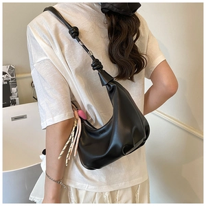 Detail view of black crescent shoulder bag featuring knotted strap and decorative charms