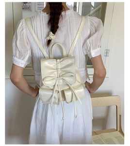 Detail of white bow drawstring backpack showing glossy leather texture and stylish bow