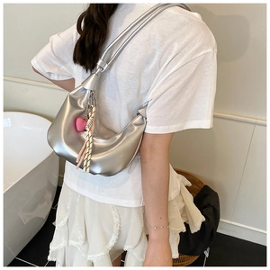 Silver metallic dumpling bag with pink heart charm shown on model in home setting