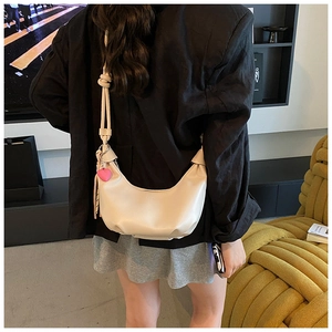 Detail of beige half-moon hobo bag featuring knotted strap and pink heart charm