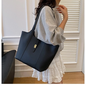 Detail of black pebbled leather tote bag featuring golden metal twist lock and dual straps