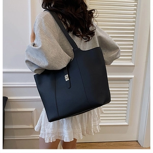 Detail of black pebbled leather tote bag with silver square buckle worn on shoulder