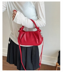 Detail of red pleated handbag featuring a knotted handle and adjustable silver buckle strap