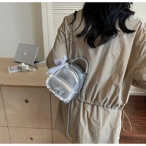 Détail d'un mini sac argenté avec bordure en dentelle blanche, nœud et chaîne de perles