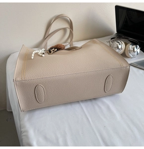 Detail of beige lychee pattern tote bag with pompom charm on a minimalist desk