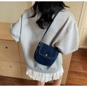 Detail of a vintage blue denim crossbody bag with a silver buckle on a young model