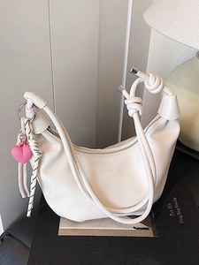 White crescent hobo bag with pink heart charm and braided strap on a minimal background