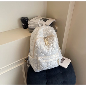 Detailed 45-degree angle view of white quilted puffer backpack with soft padded texture
