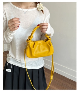 Detail of soft yellow pleated crossbody bag with knotted handle worn by a model