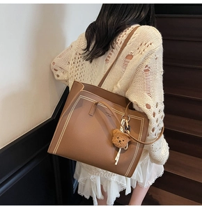 Detail of large brown tote bag with litchi texture and cute bear charm on shoulder