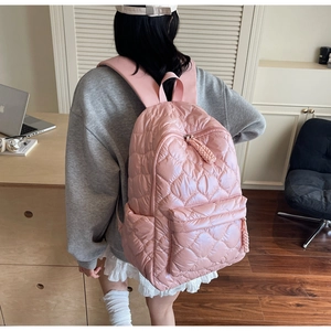Rear view of a light pink quilted puffer backpack shown on a model in a home setting