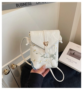 Close-up of white lace floral embroidery and heart-shaped gold clasp on phone bag