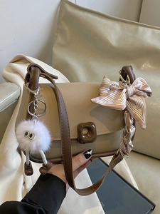Borsa a tracolla beige con bordo marrone, fiocco in seta e ciondolo di peluche