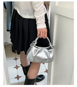 Silver pleated cloud bag with knotted handle shown in a stylish hand-held fashion pose