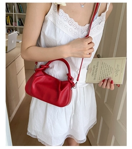 Close-up of red pleated handbag with knot handle detail and adjustable strap