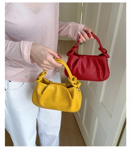 Detail of red and yellow pleated handbags featuring unique knotted handles and soft textures