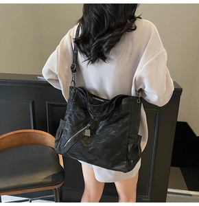 Detail of large black textured tote bag featuring a side zipper and adjustable strap
