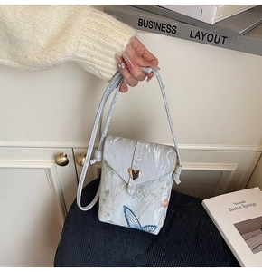 Detail of embroidered floral lace mini phone bag with golden heart clasp and slim strap