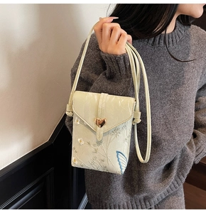Detail of floral and butterfly embroidery on a crossbody phone bag with gold heart buckle
