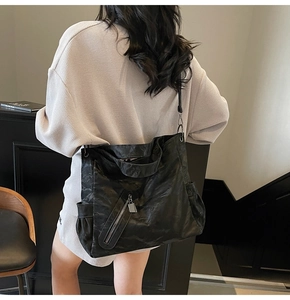Detail of black pleated leather tote bag with metallic zipper on a shoulder-worn model