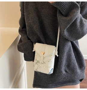 Detail of floral embroidery and gold heart clasp on a white leather crossbody bag
