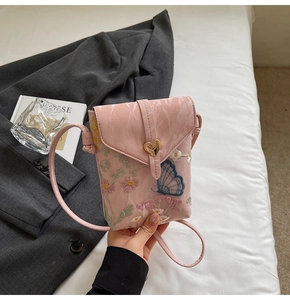 Detailed embroidery of flowers and blue butterfly on a mini leather crossbody phone bag