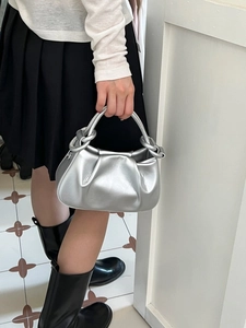 Silver metallic handbag with large knot handle and pleated modern texture on model