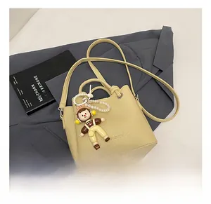 Detalle de bolso tipo cubo crema con colgante de muñeca y textura de cuero lichi