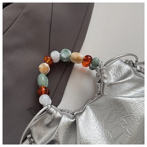 Detail of silver metallic cloud bag featuring textured pleats and colored bead handle