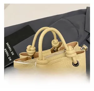 Detalle del bolso de cubo beige con asas anudadas y cierre de cremallera metálica