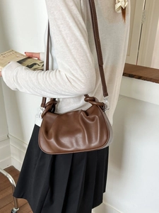 Brown soft leather croissant bag with knotted handle and shoulder strap in a lifestyle setting