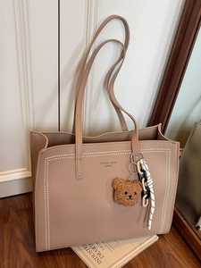 Minimalist beige pebble leather tote bag with a plush bear charm for daily commuting