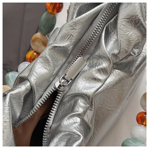 Detail of silver metallic pleated handbag with colorful bead handle and silver zipper