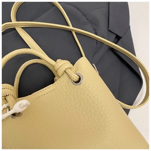 Detail of yellow lychee leather bucket bag with drawstring handle on a blue blazer