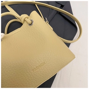 Detail of lychee pattern leather bucket bag in cream yellow with embossed fashion text