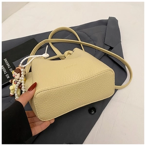Close-up of beige pebble grain leather bucket bag featuring a pearl doll charm