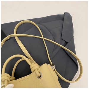 Detail of cream yellow lychee grain leather bucket bag with knotted handle and strap