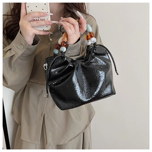 Detail of black patent leather bucket bag with colorful acrylic pearl handle and drawstrings