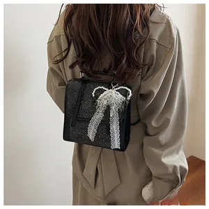 Detail of black PU backpack with silver star patch and a pearl lace bow pendant