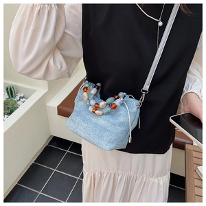 Detail of light blue textured bucket bag featuring colorful resin bead handle and shoulder strap