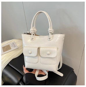 Detail of cream crocodile textured handbag with woven knot handle and front pockets