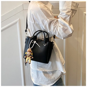 Detail of black lychee grain leather bucket bag with cute doll charm and shoulder strap