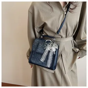 Close-up of blue denim handbag featuring a large lace bow and pearl chain detail