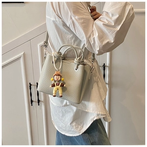 Detail of grey-green leather bucket bag with knot handle and girl charm worn by model