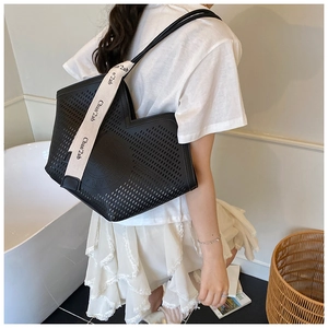 Detail of black laser-cut tote bag with wide white canvas strap on shoulder