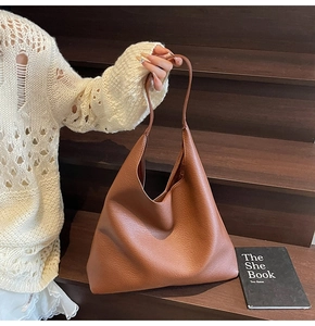 Detail einer braunen Tote-Bag aus Leder mit Lychee-Muster, getragen auf Holzstufen