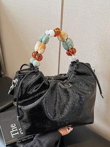 Glossy black pleated bucket bag with a colorful beaded handle and drawstring closure