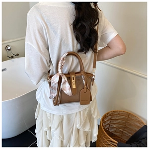 Détail d'un sac seau en cuir marron et PVC avec foulard en soie sur tenue blanche
