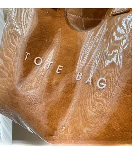 Detailed macro shot of a brown PVC tote bag featuring high-gloss texture and bold white text