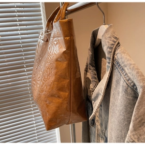 Detail of glossy patent leather tote bag in dark brown hanging on a metal rack